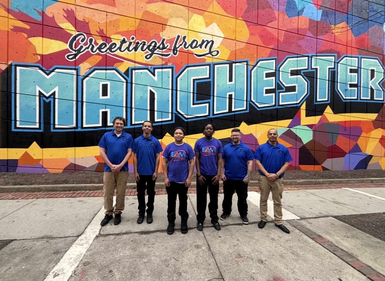 The EAM Moving crew in Manchester, NH in front of the Greetings from Manchester mural